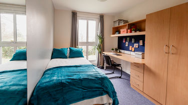 Student bedroom with a single bed, desk, and wardrobe. There is a large floor to ceiling window. 